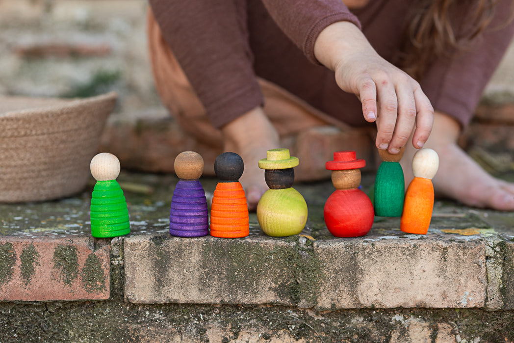 Colorful wooden peg dolls on a stone surface with a person interacting with them.