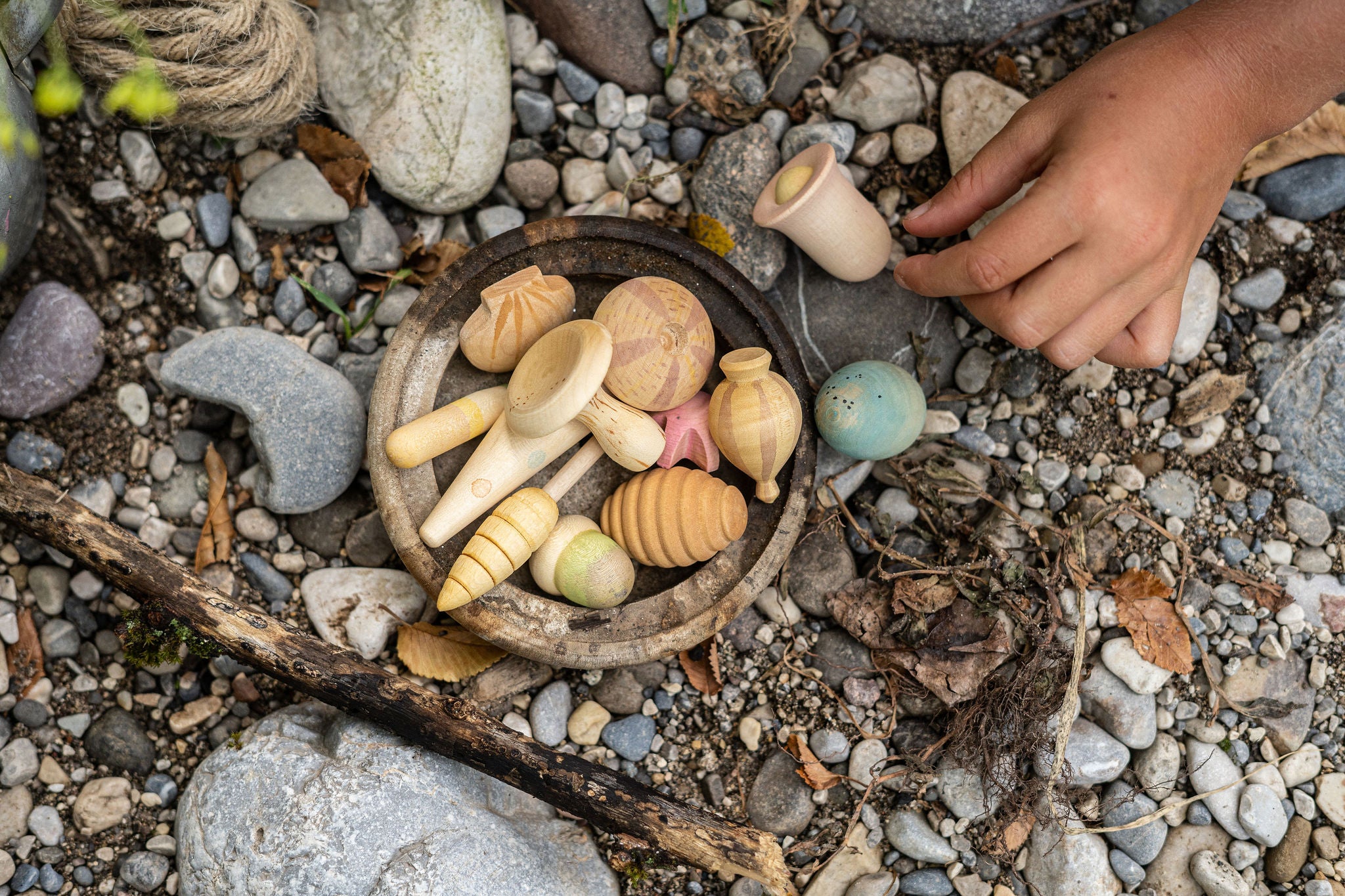 Wooden toys on pebbles with a hand reaching towards them