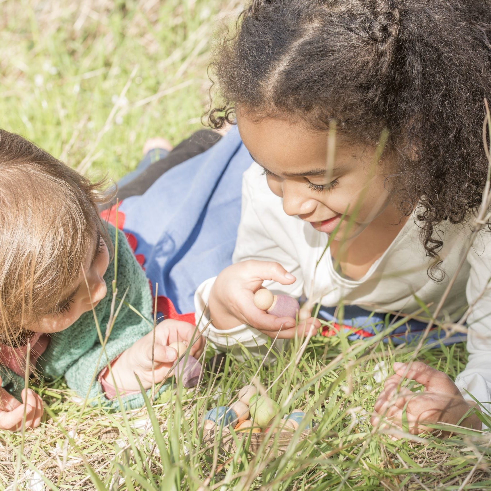Two children lying on the grass, exploring nature together.