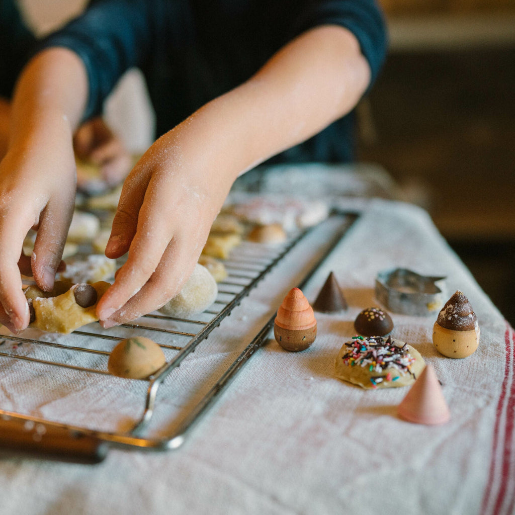 Child decorating cookies on a cooling rack with various toppings.