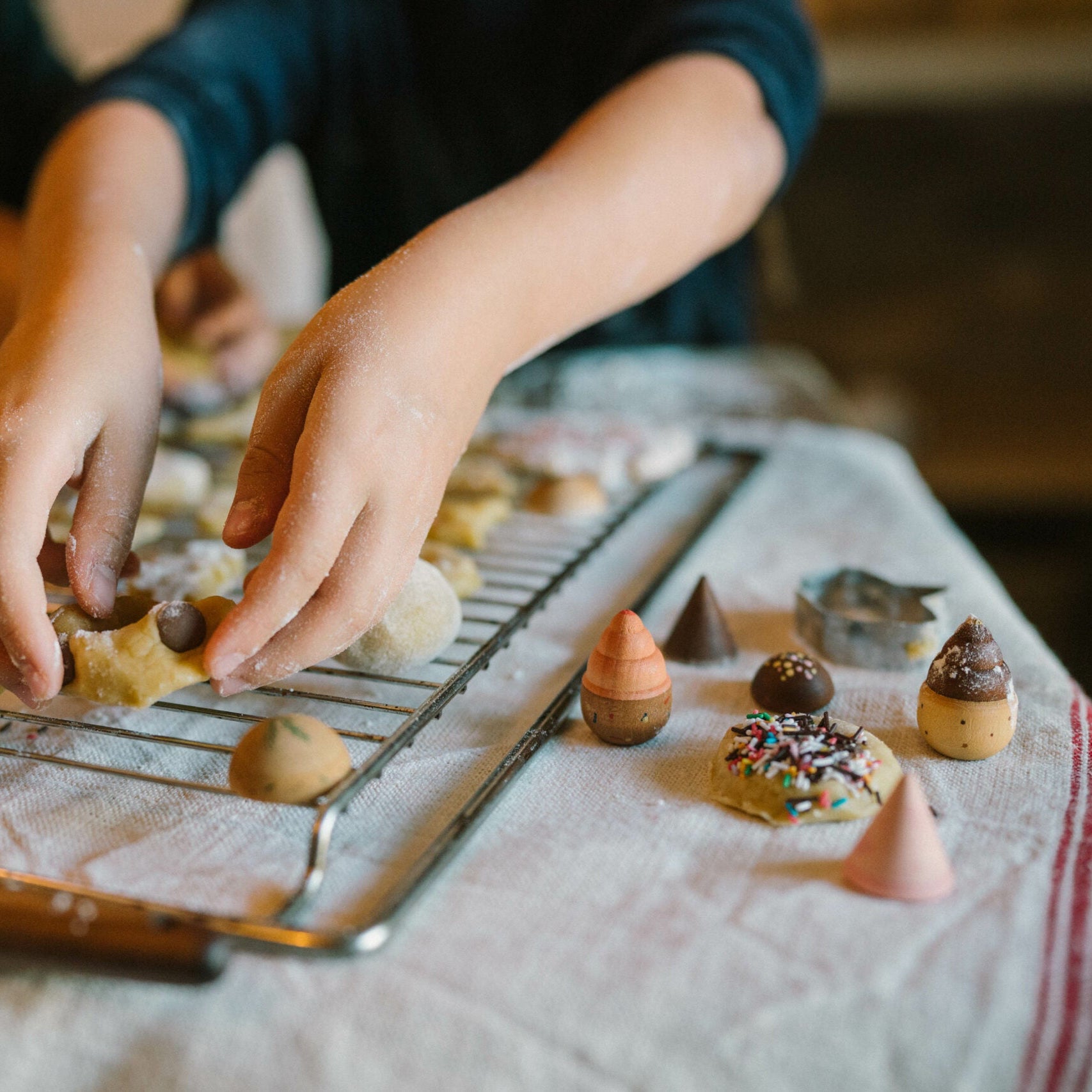 Child decorating cookies on a cooling rack with various toppings.