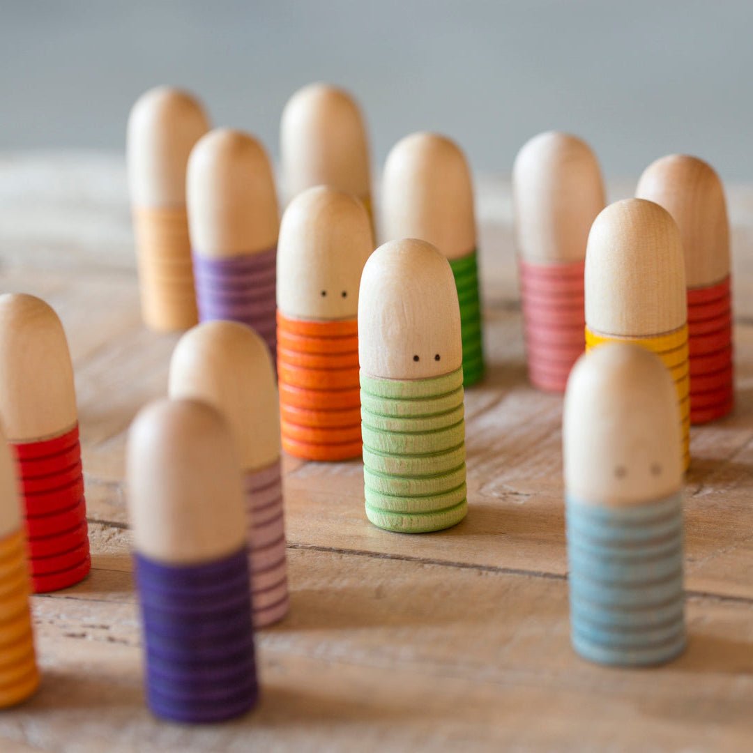 Colorful wooden toys resembling people on a wooden surface with a basket in the background.