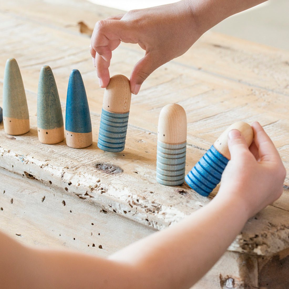 Children's hands playing with wooden and ceramic shape sorting toys on a wooden surface.
