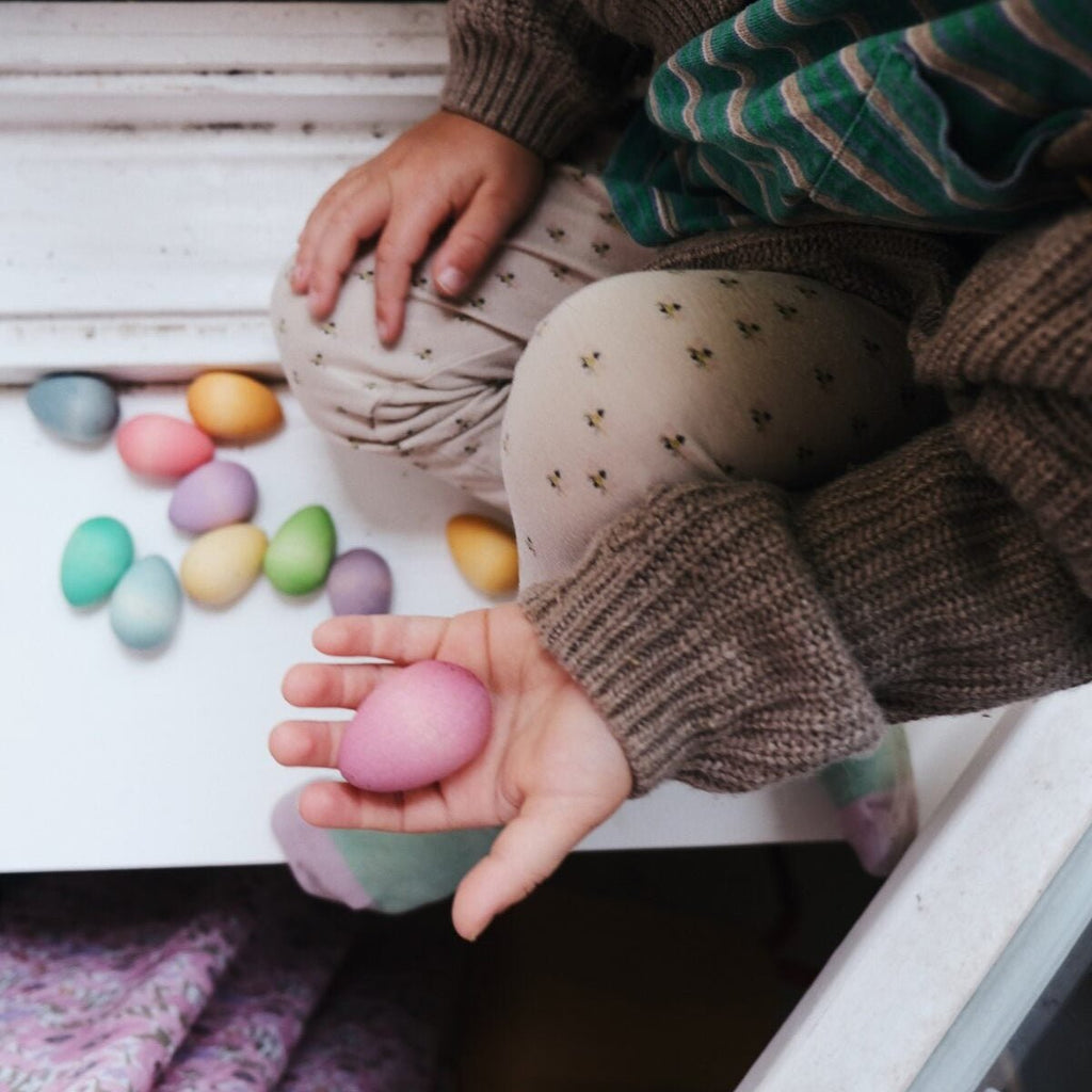 Child holding a pink Easter egg with colorful eggs on a wooden surface