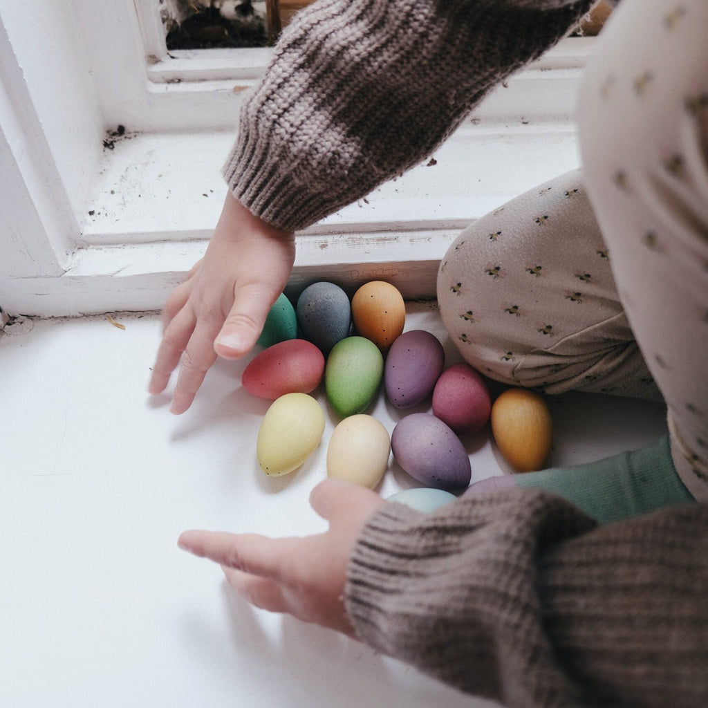 Child playing with colorful eggs near a window