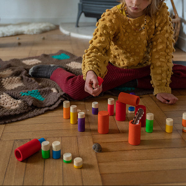 Child playing with colorful toys on a wooden floor in front of a fireplace.