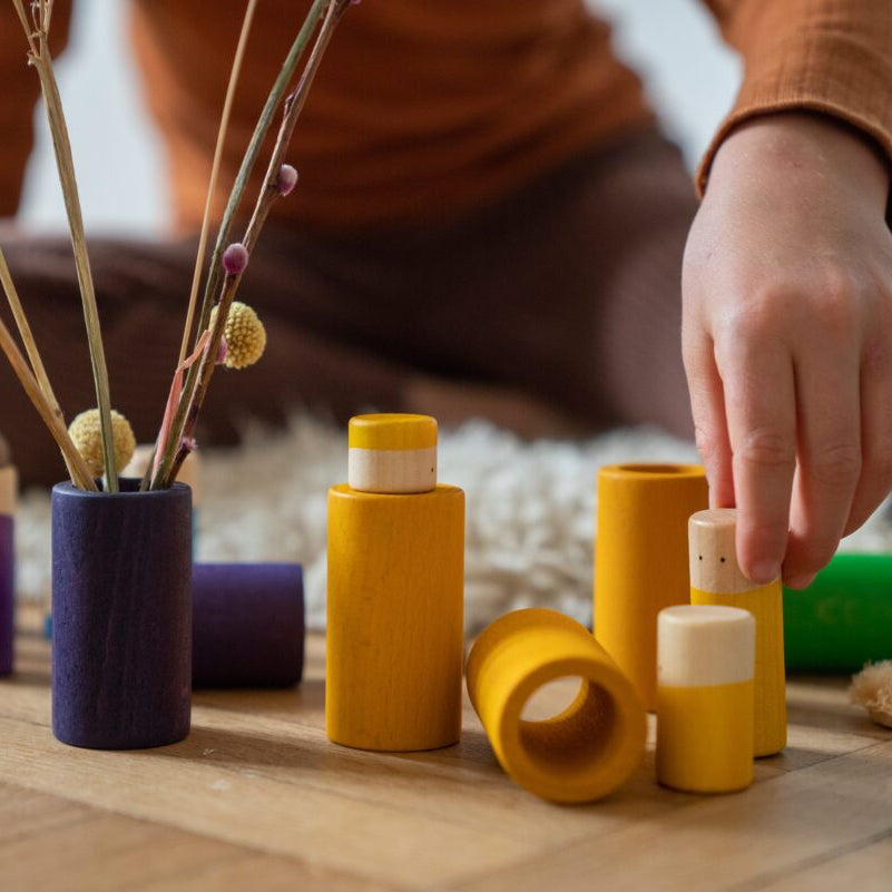 Colorful wooden toys on a wooden floor with a blurred person in the background.