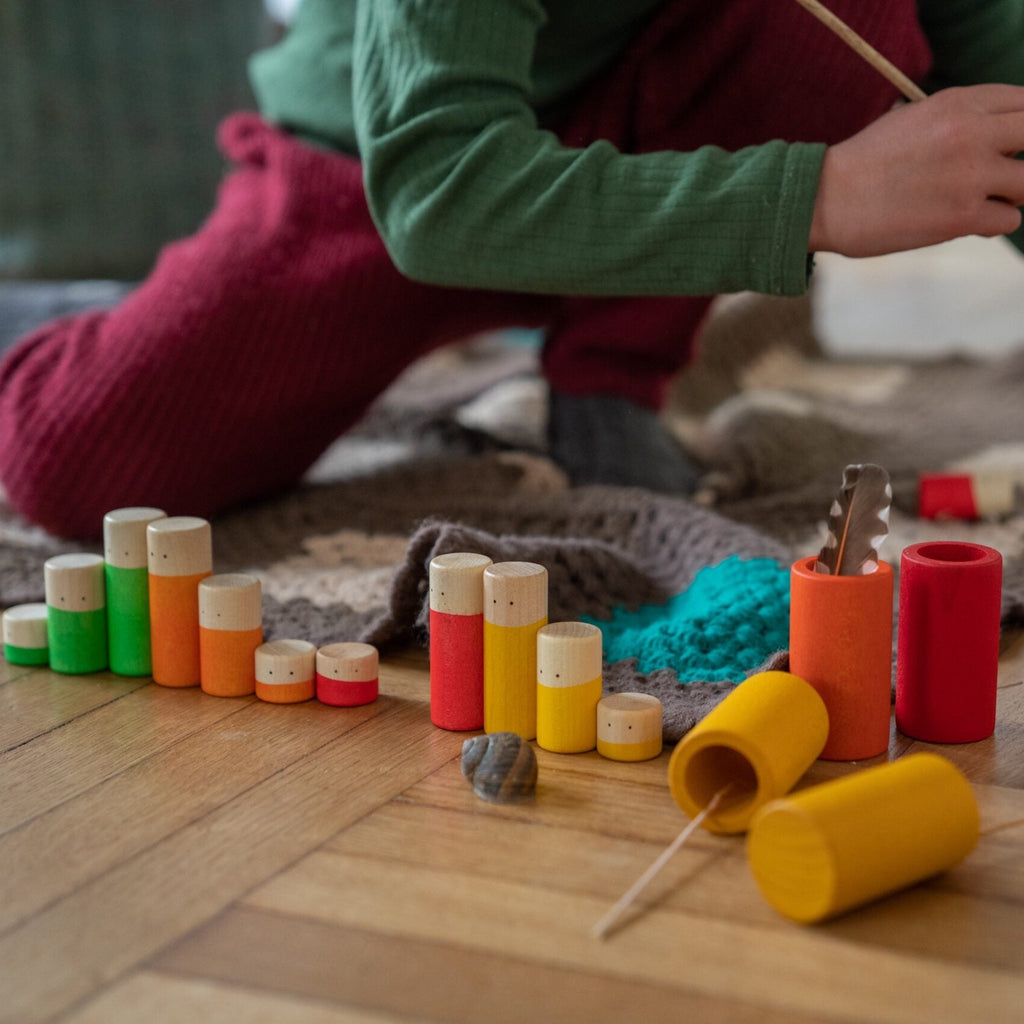 Child playing with colorful cylindrical toys on a wooden floor.