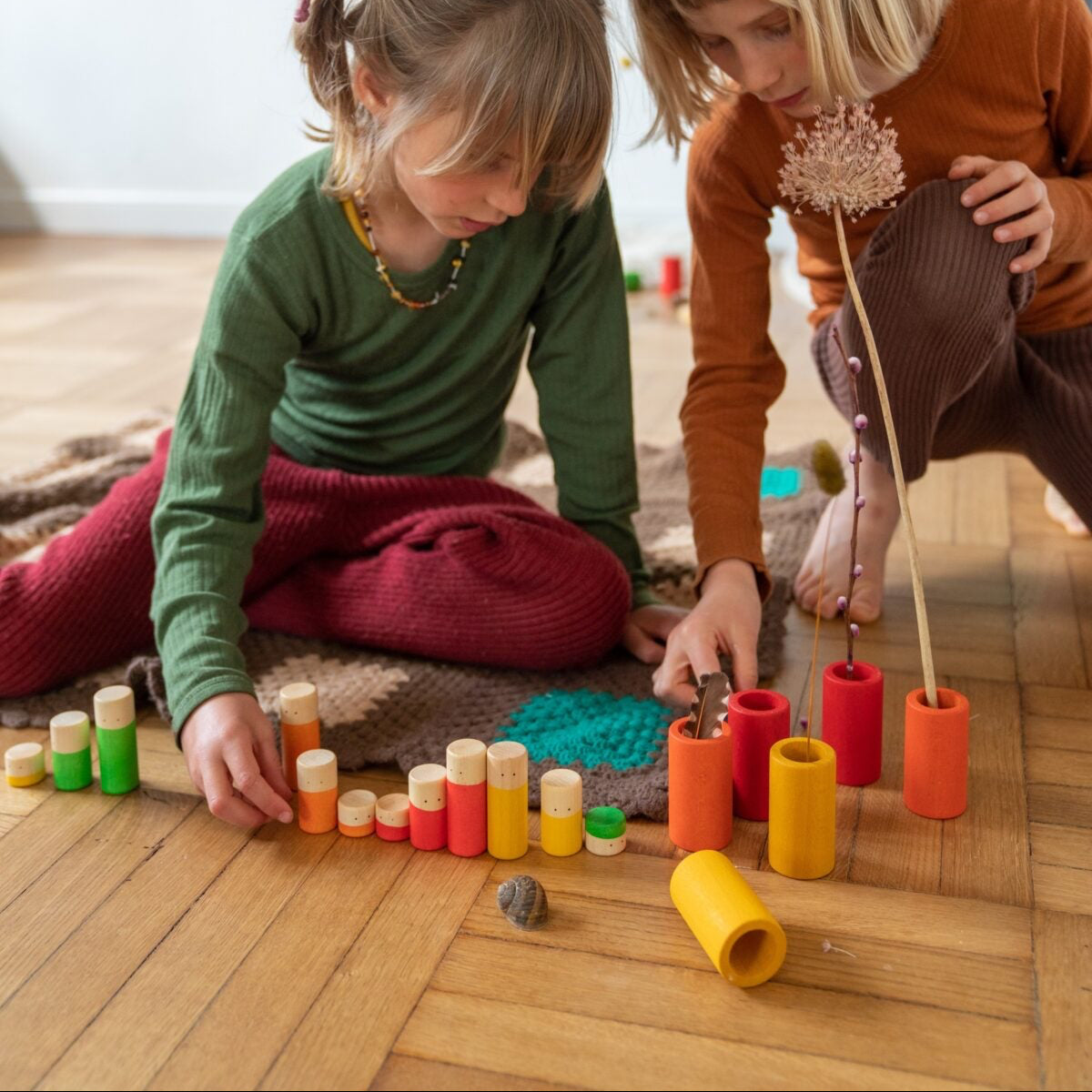 Two children playing with colorful toys on a wooden floor.
