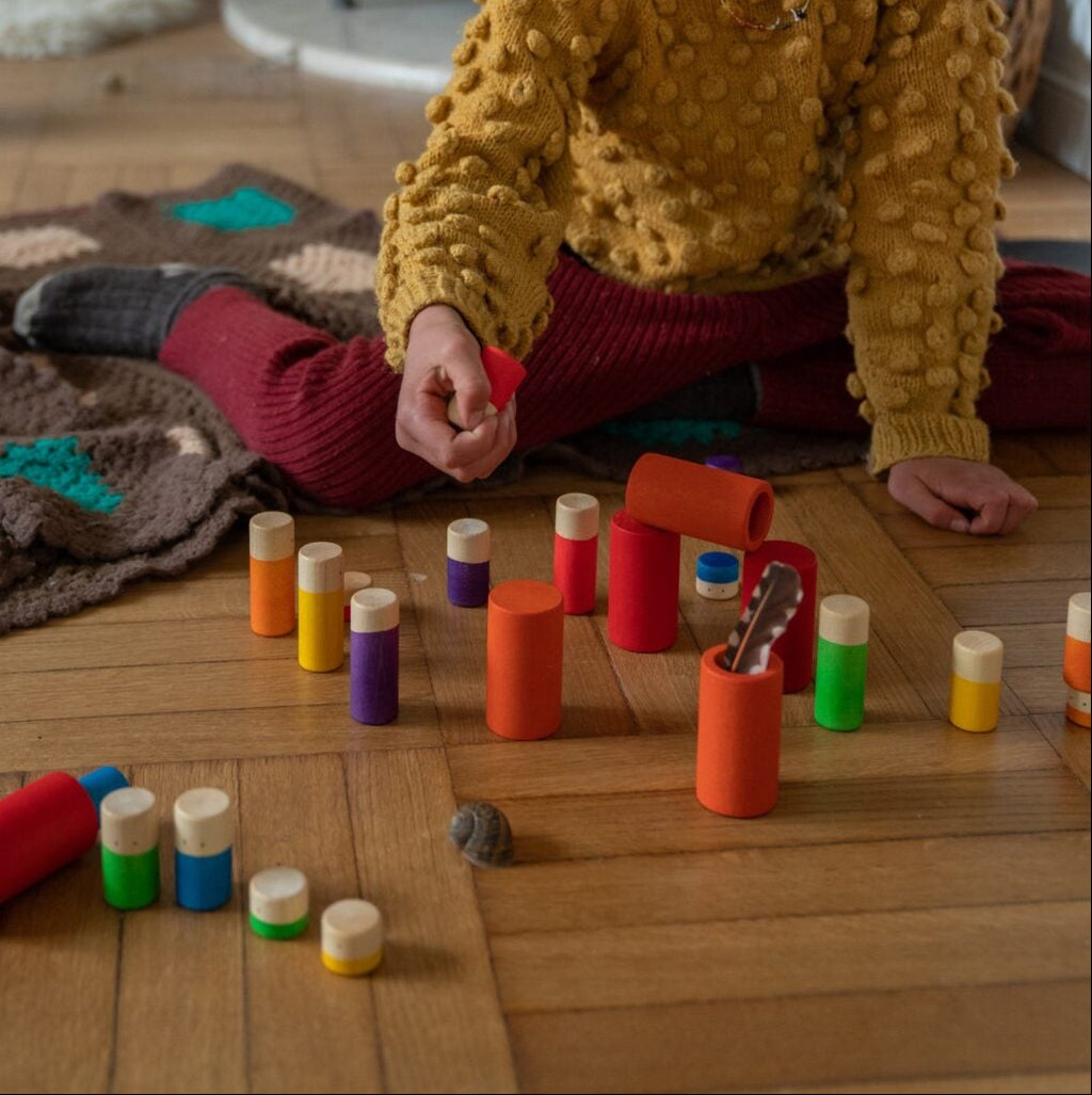 Child playing with colorful toys on a wooden floor in front of a fireplace.