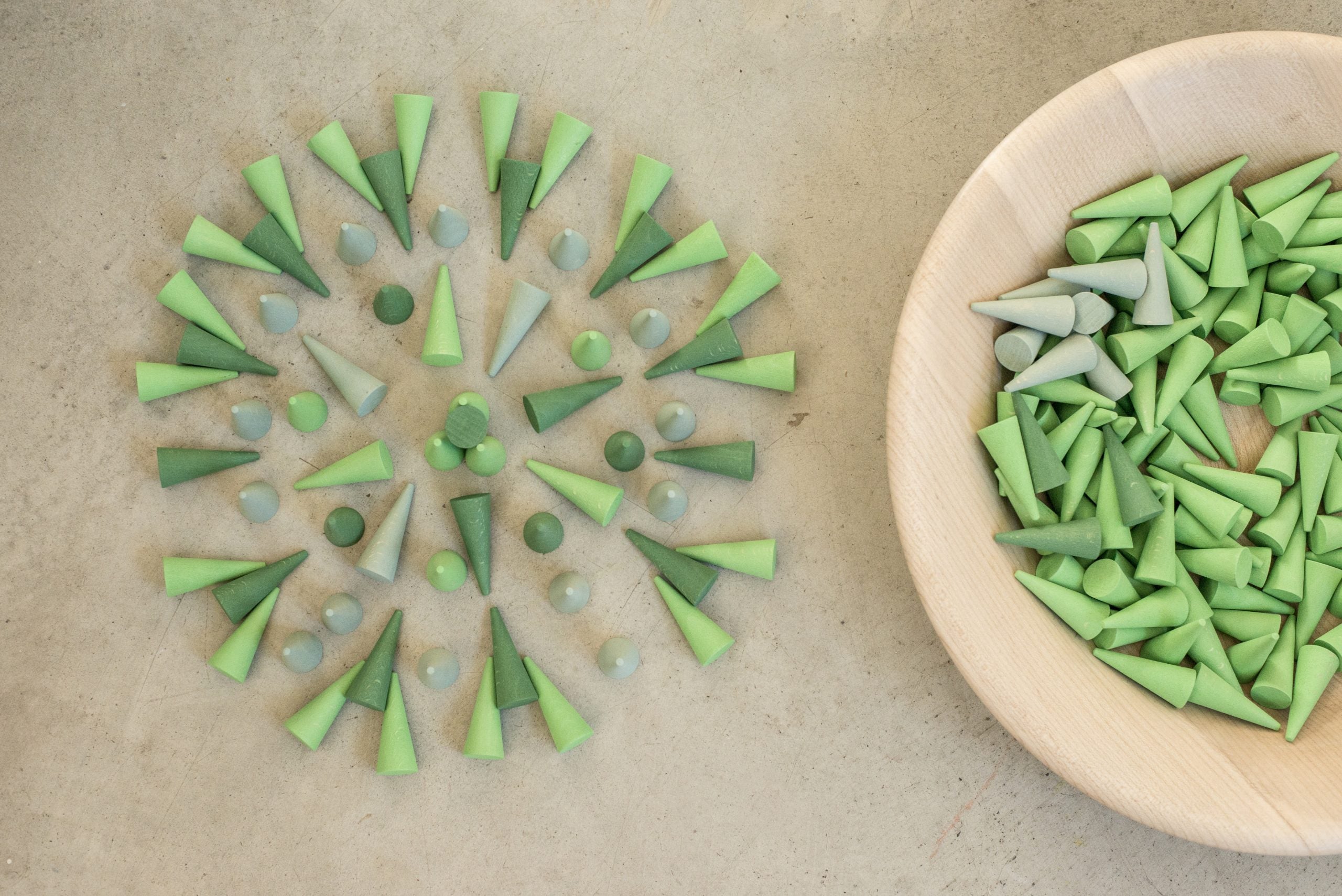 Decorative arrangement of green and gray cone-shaped objects on a beige surface with a bowl of additional objects.