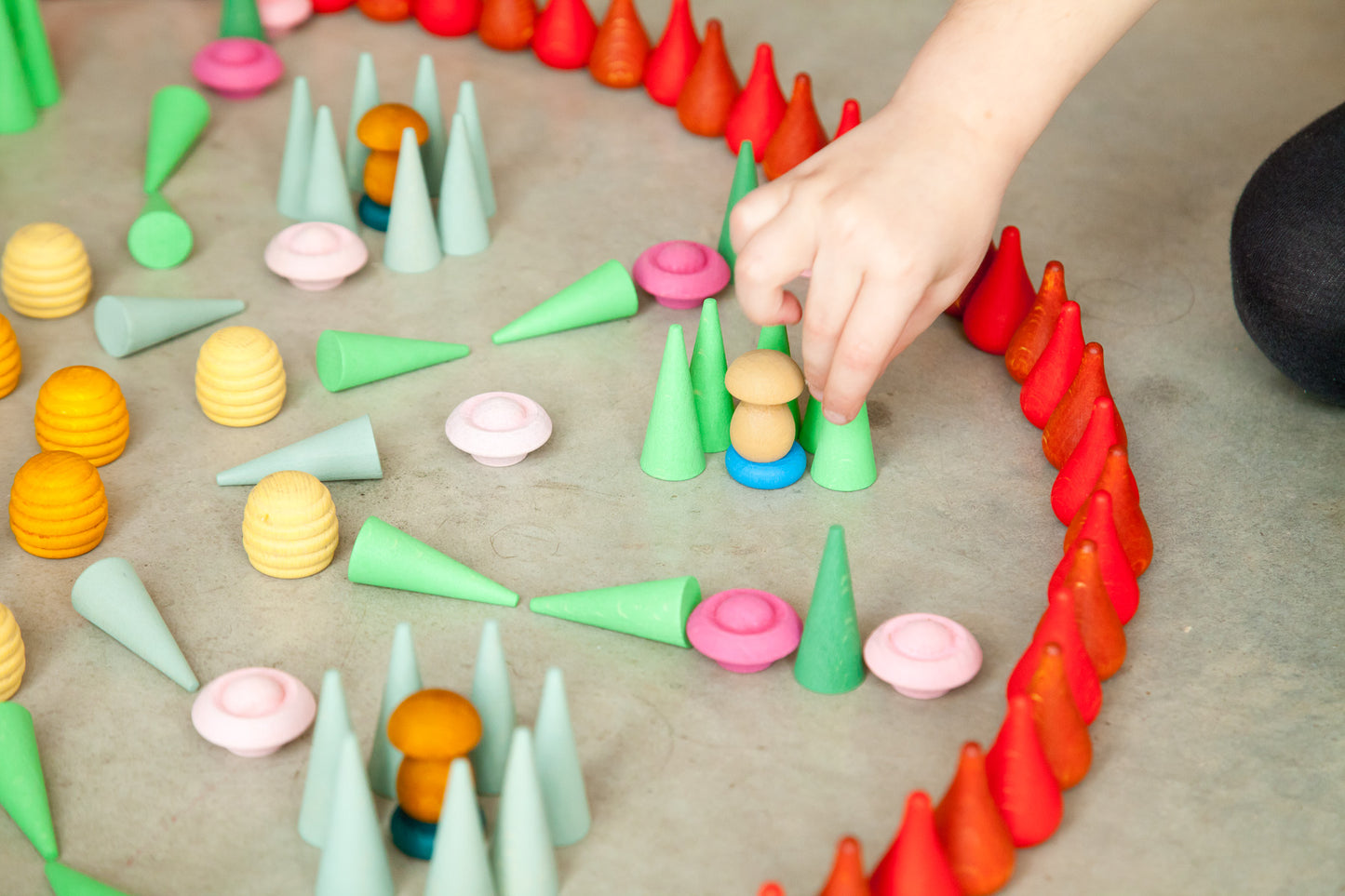 Colorful geometric shapes arranged in a circular pattern on a flat surface, with a hand interacting with them.