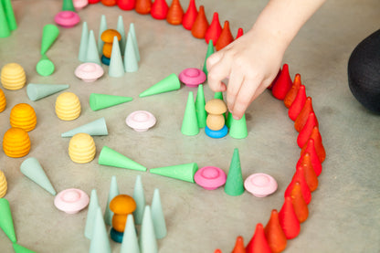 Colorful geometric shapes arranged in a circular pattern on a flat surface, with a hand interacting with them.