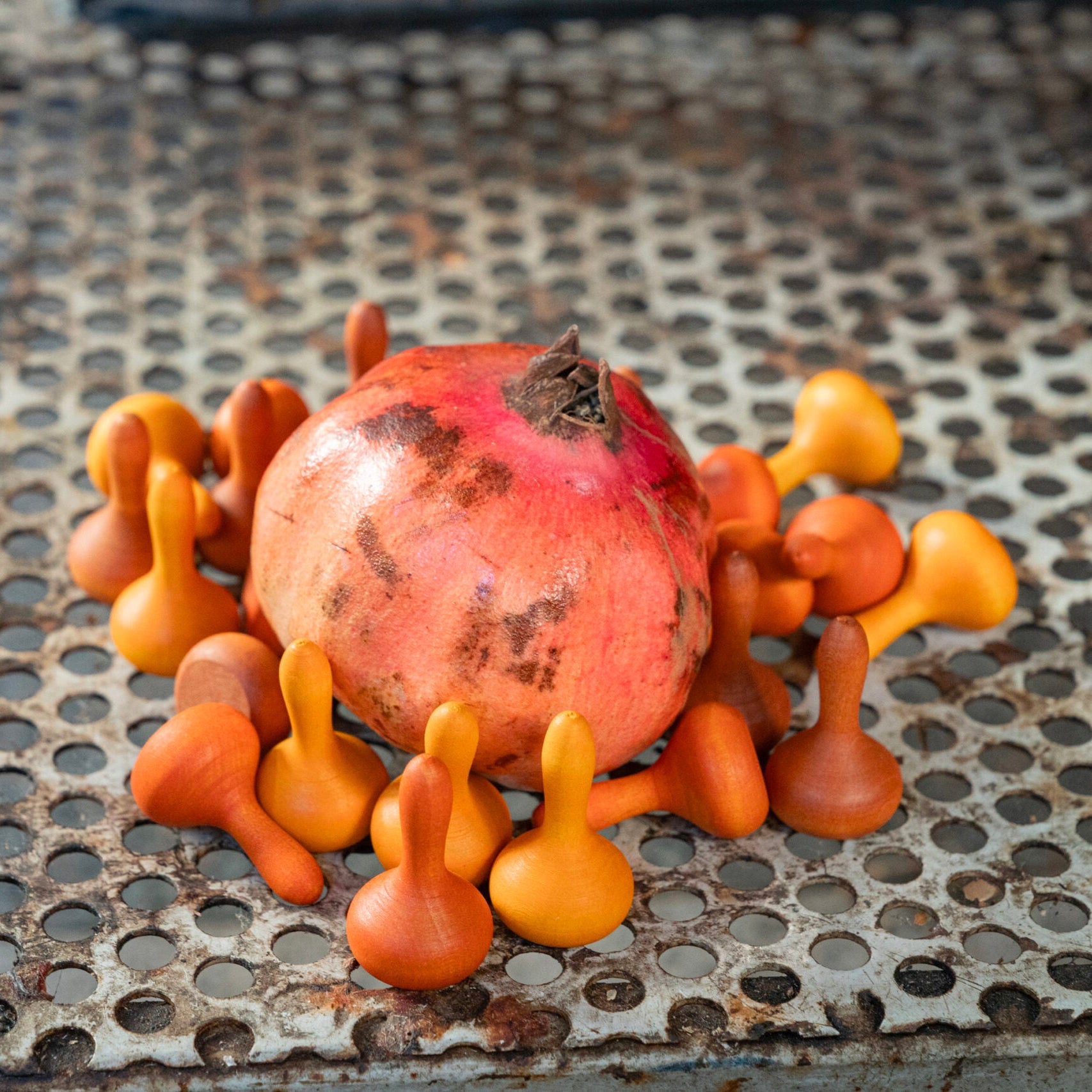 Pomegranate surrounded by orange and yellow gumball-like objects on a metal surface