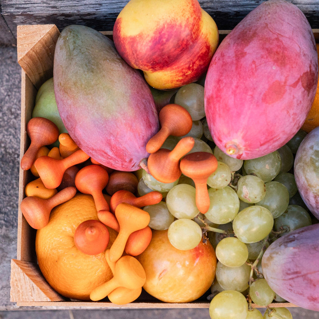 Box of assorted fruits including mangoes, grapes, and apples on a stone surface.