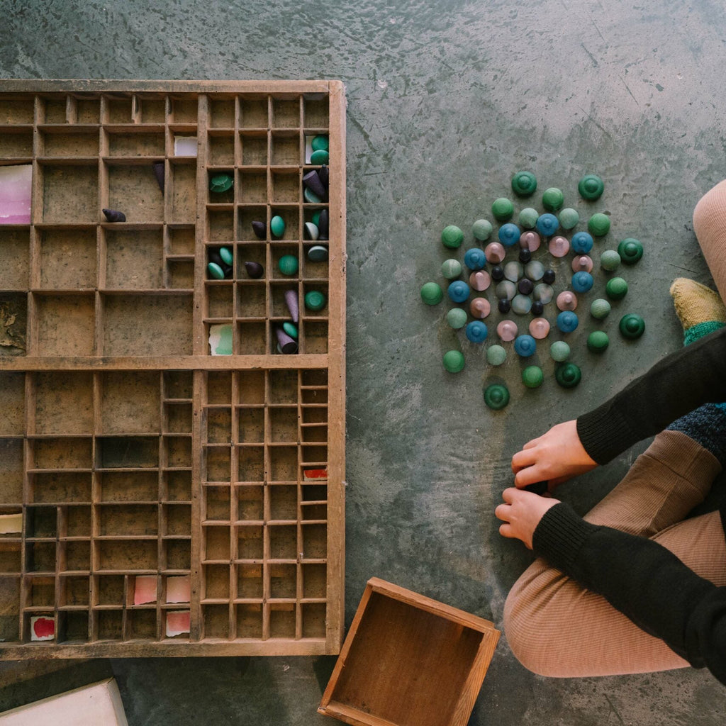 Person sitting on the floor with a wooden letterpress tray and colorful objects.