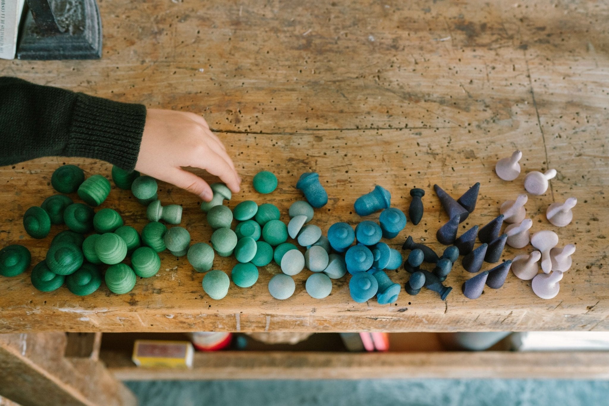 Colorful clay sculptures on a wooden table with a hand reaching out.