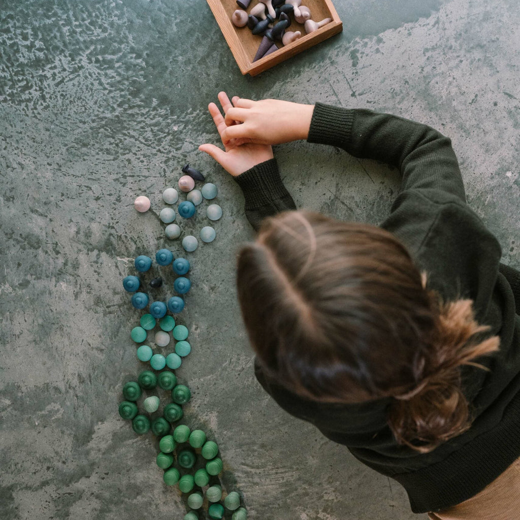 Person arranging colorful mandala on a textured surface with a wooden box nearby.