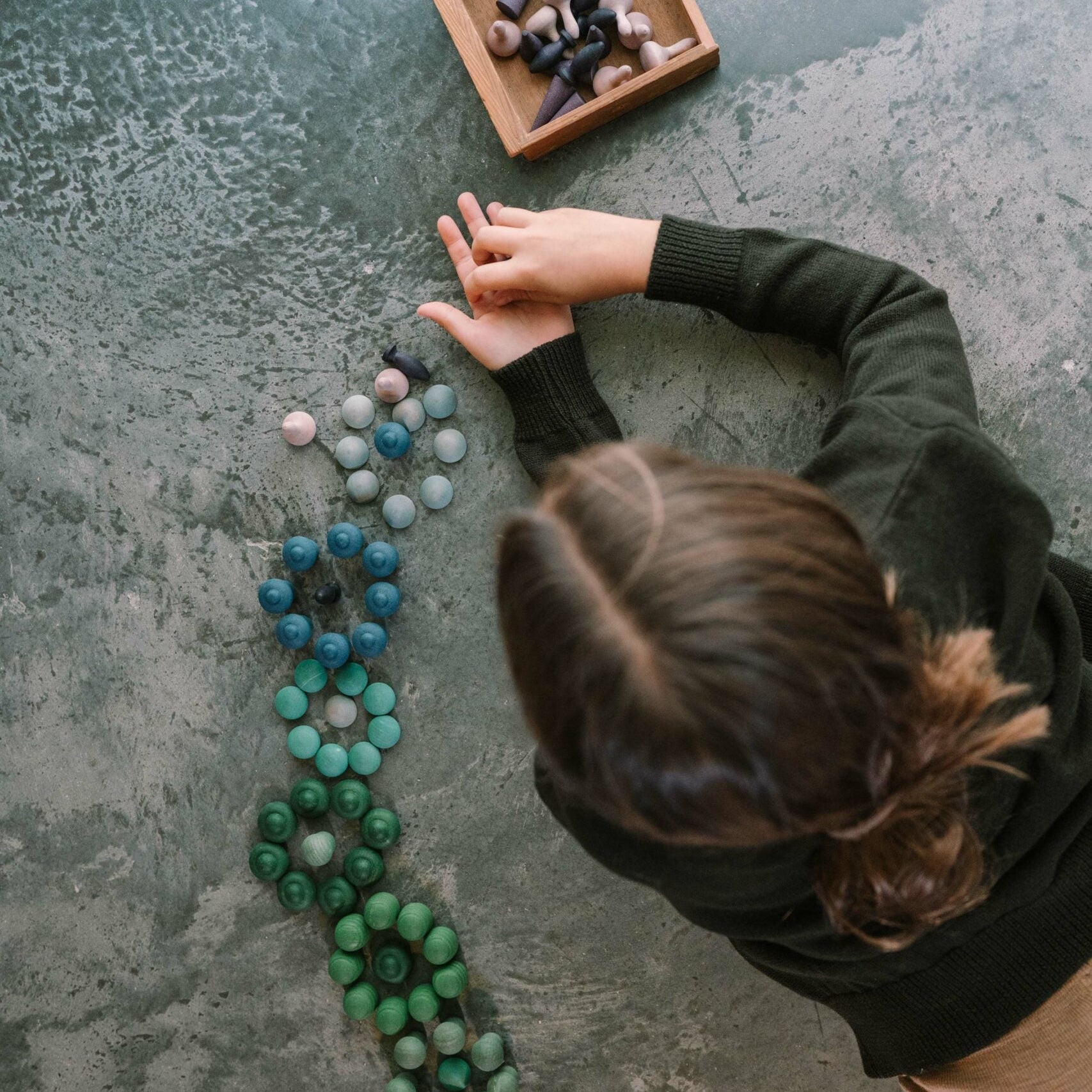Person arranging colorful mandala on a textured surface with a wooden box nearby.