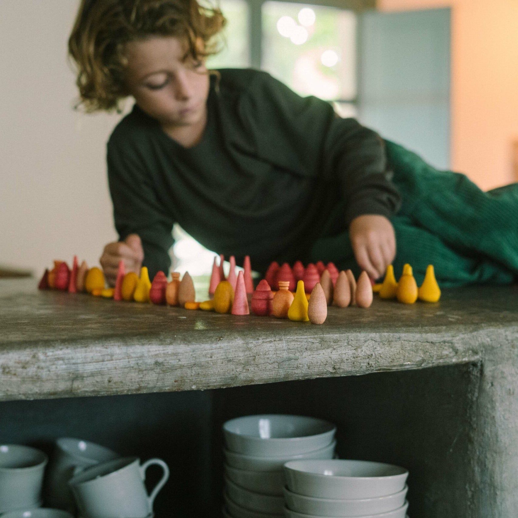 Person arranging colorful ceramic figurines on a stone surface with kitchenware in the background.