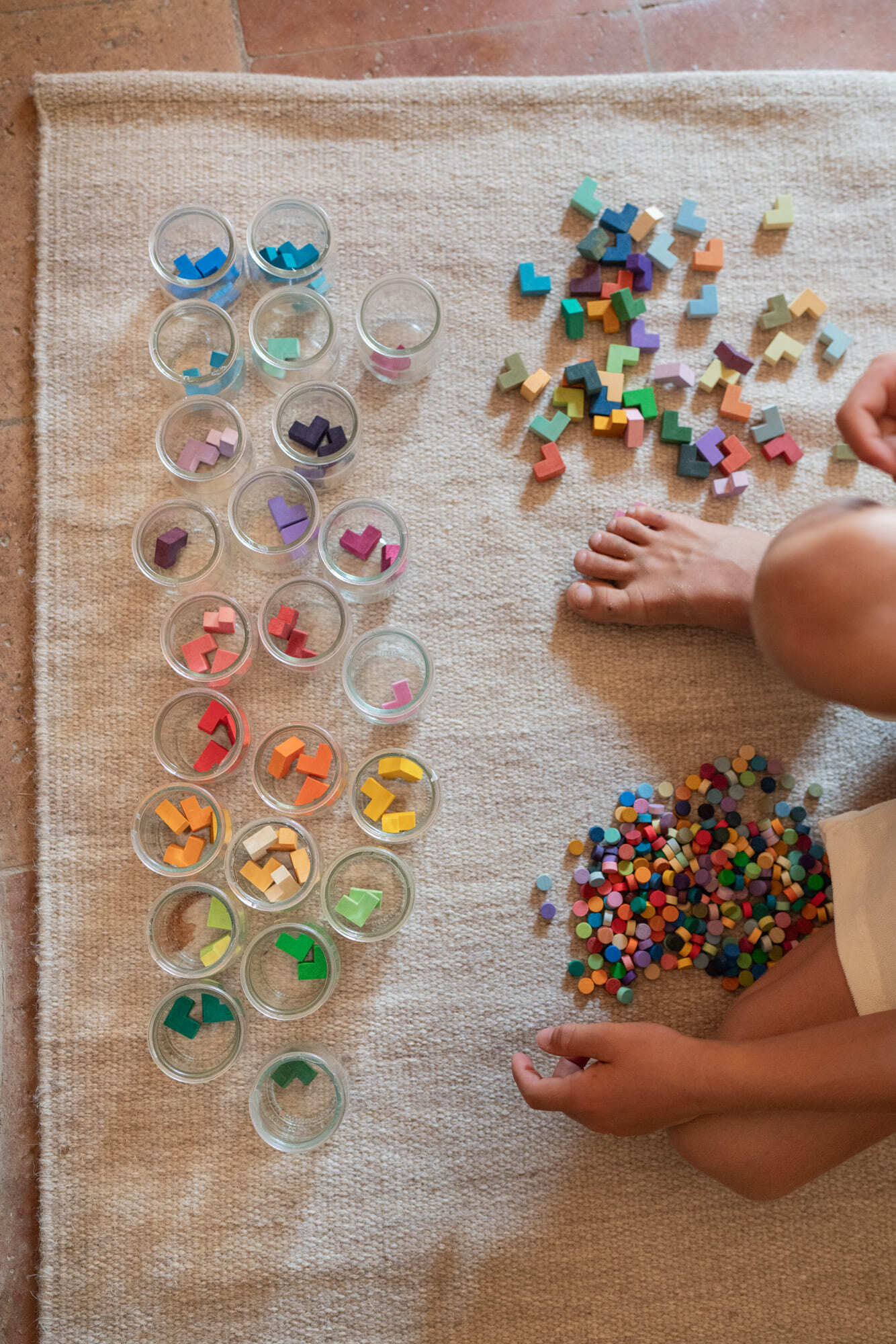 Colorful wooden letters on a mat with clear containers and child's hands