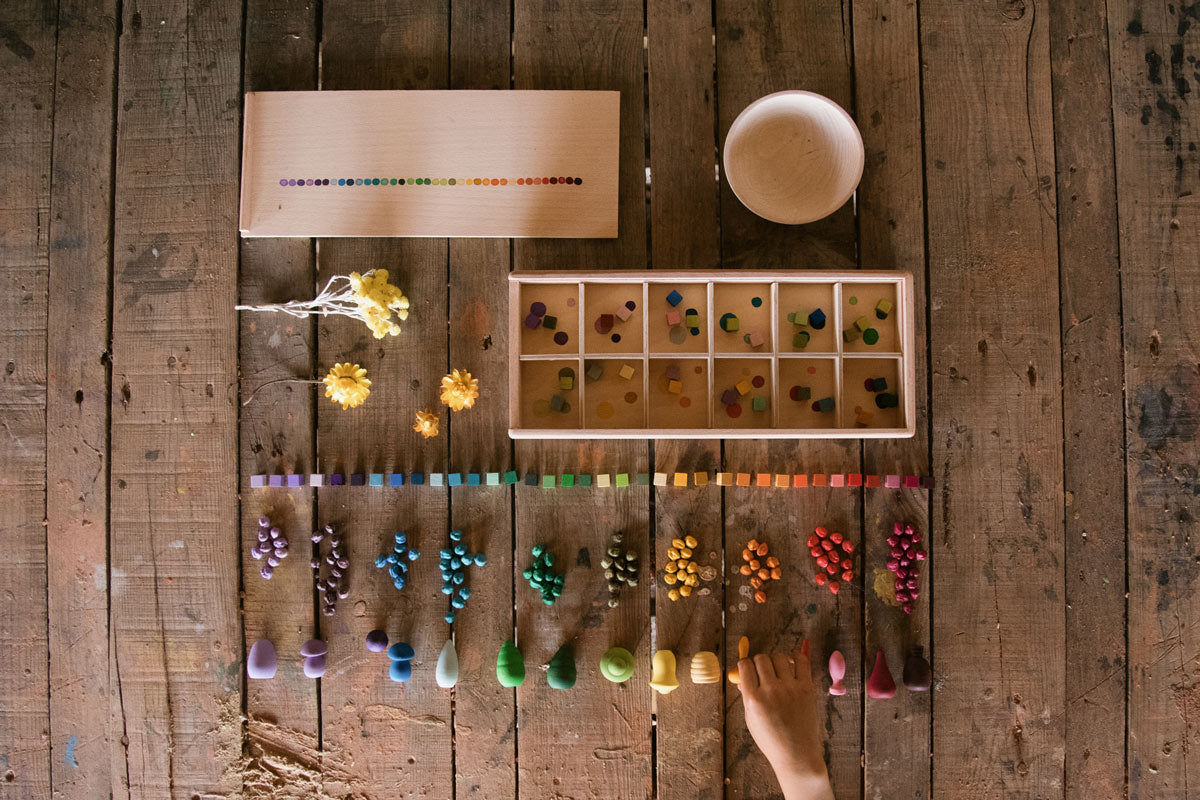 Color sorting activity on a wooden table with various colored objects and tools.