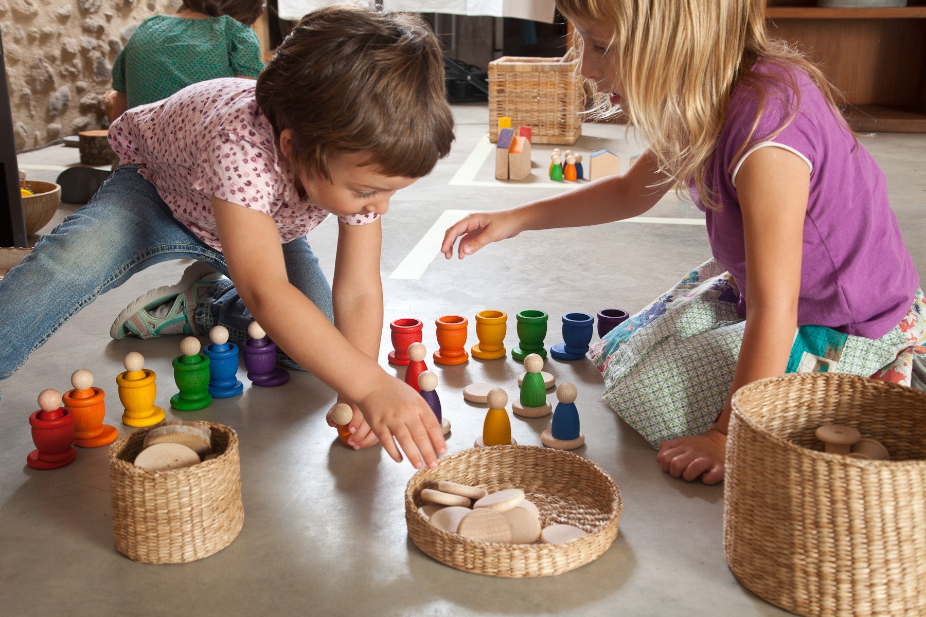 Two children playing with colorful toys on a concrete floor.