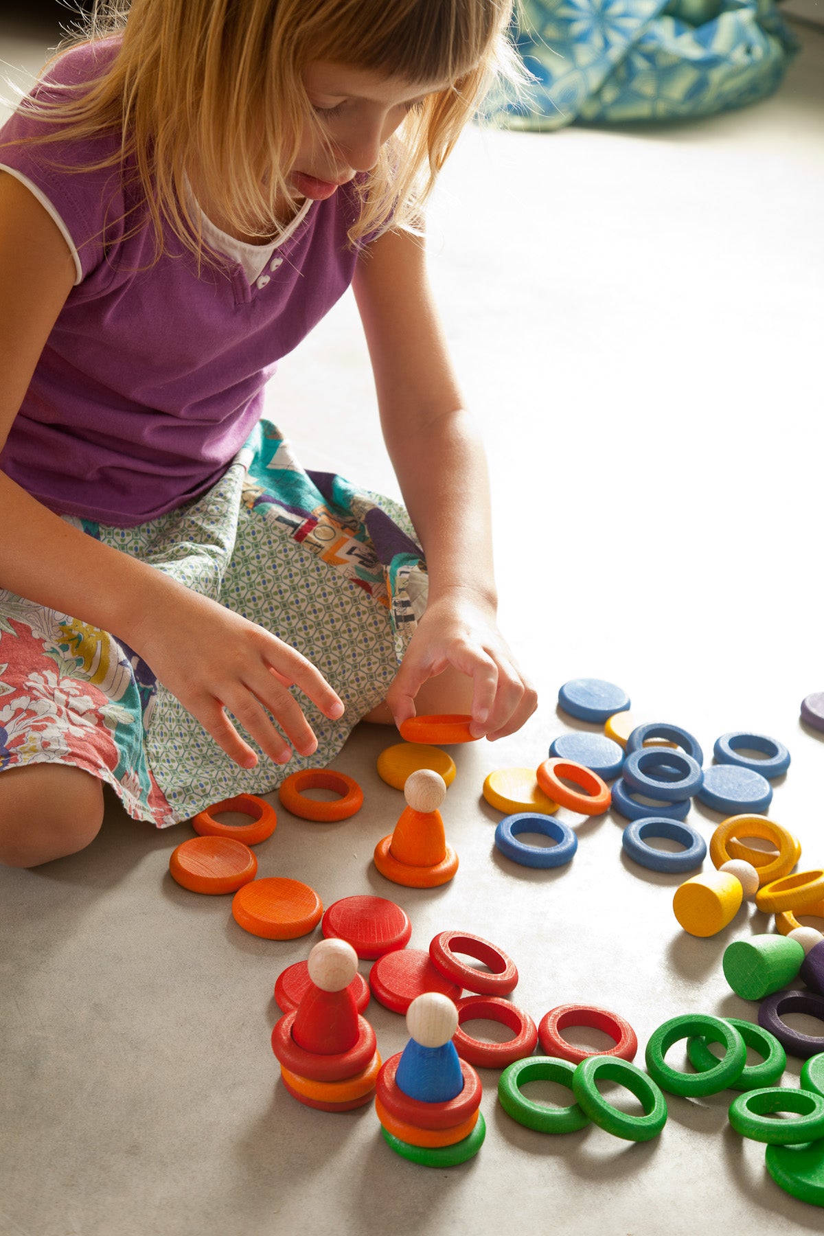 Child playing with colorful toy rings on a light-colored floor.