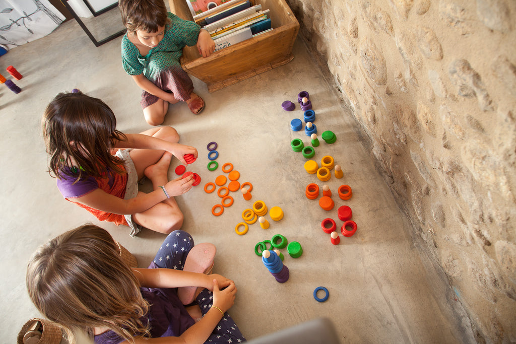 Three children playing with colorful toys on a stone floor.