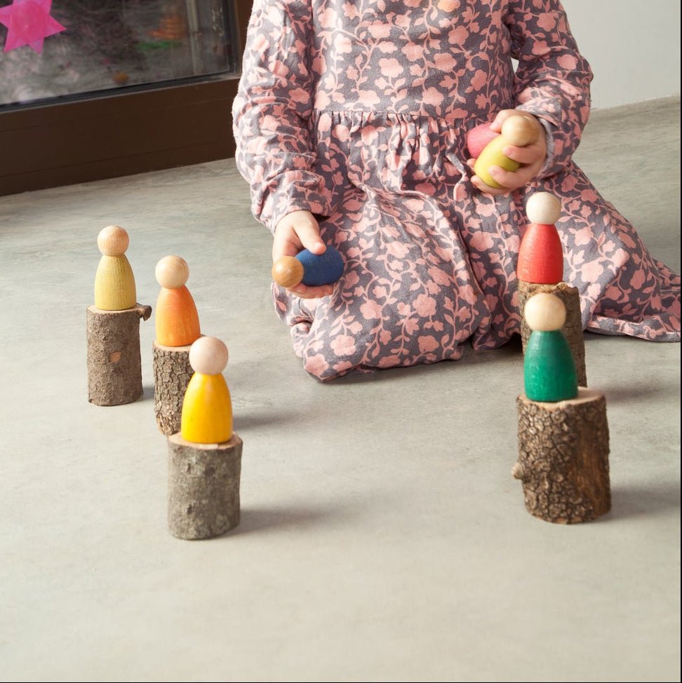 Child playing with colorful wooden peg dolls on a light surface.
