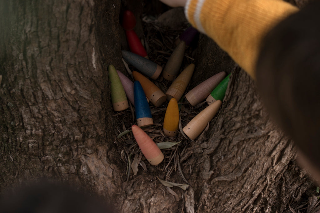 Colorful wooden toys in a nest with a hand reaching in, set against a natural background.