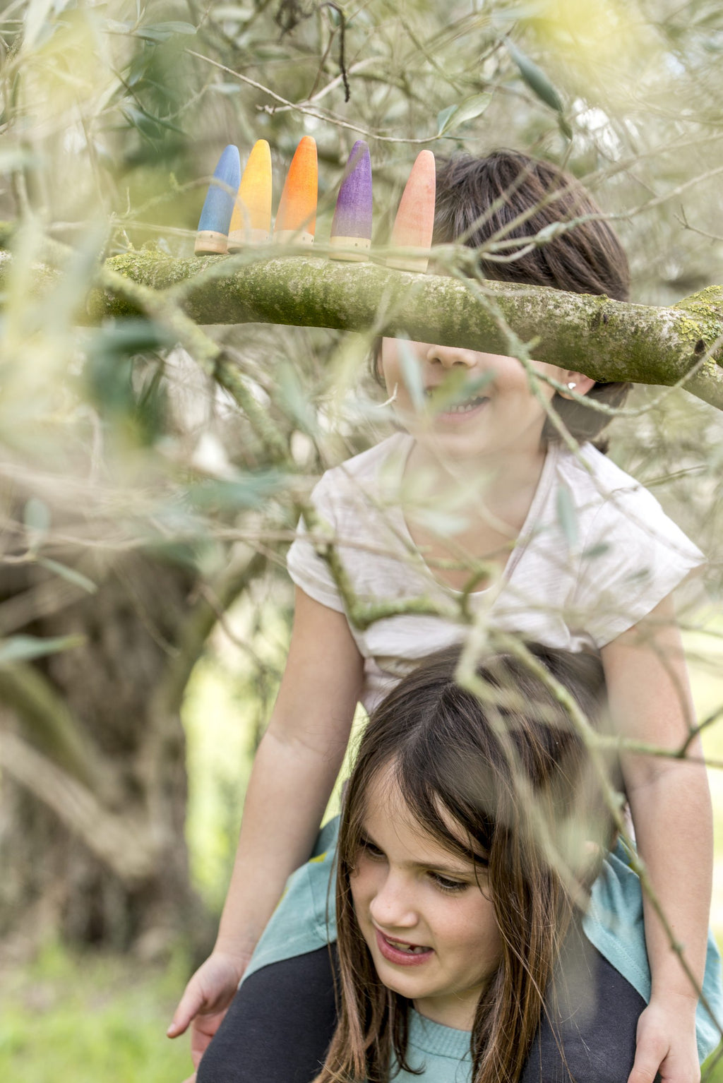 Two children playing outdoors with colorful sticks, surrounded by greenery.