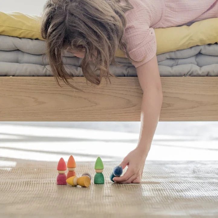 Child playing with colorful wooden toys on a light wooden floor.