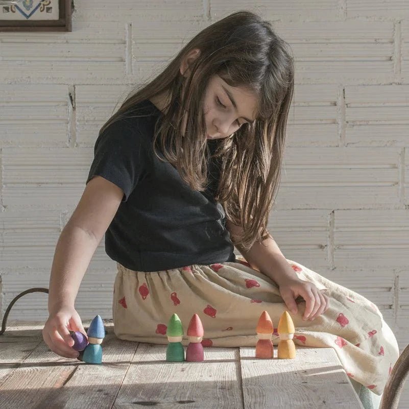 Young girl playing with colorful wooden toys on a table against a light wooden paneled wall.