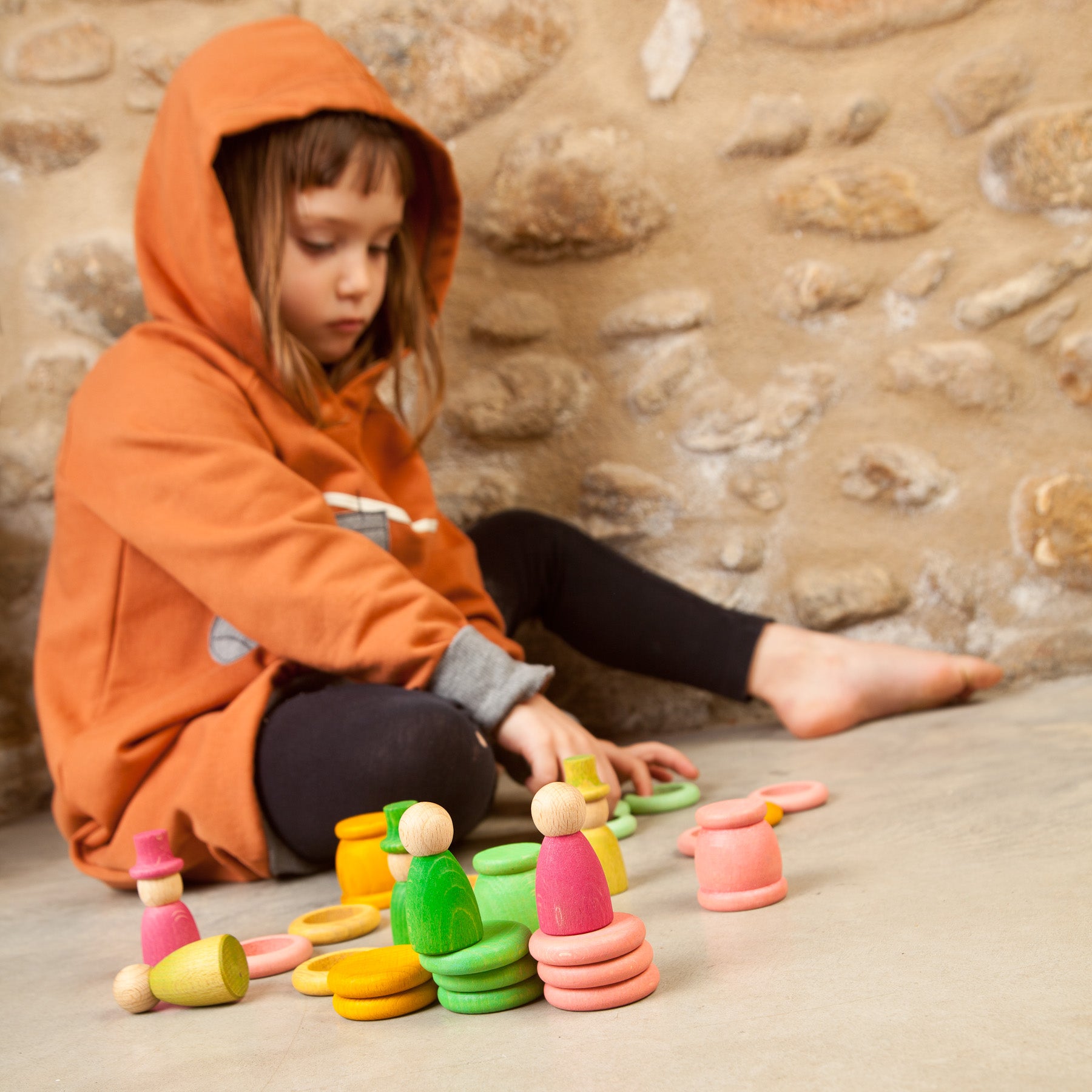 Child playing with colorful wooden toys against a stone wall background