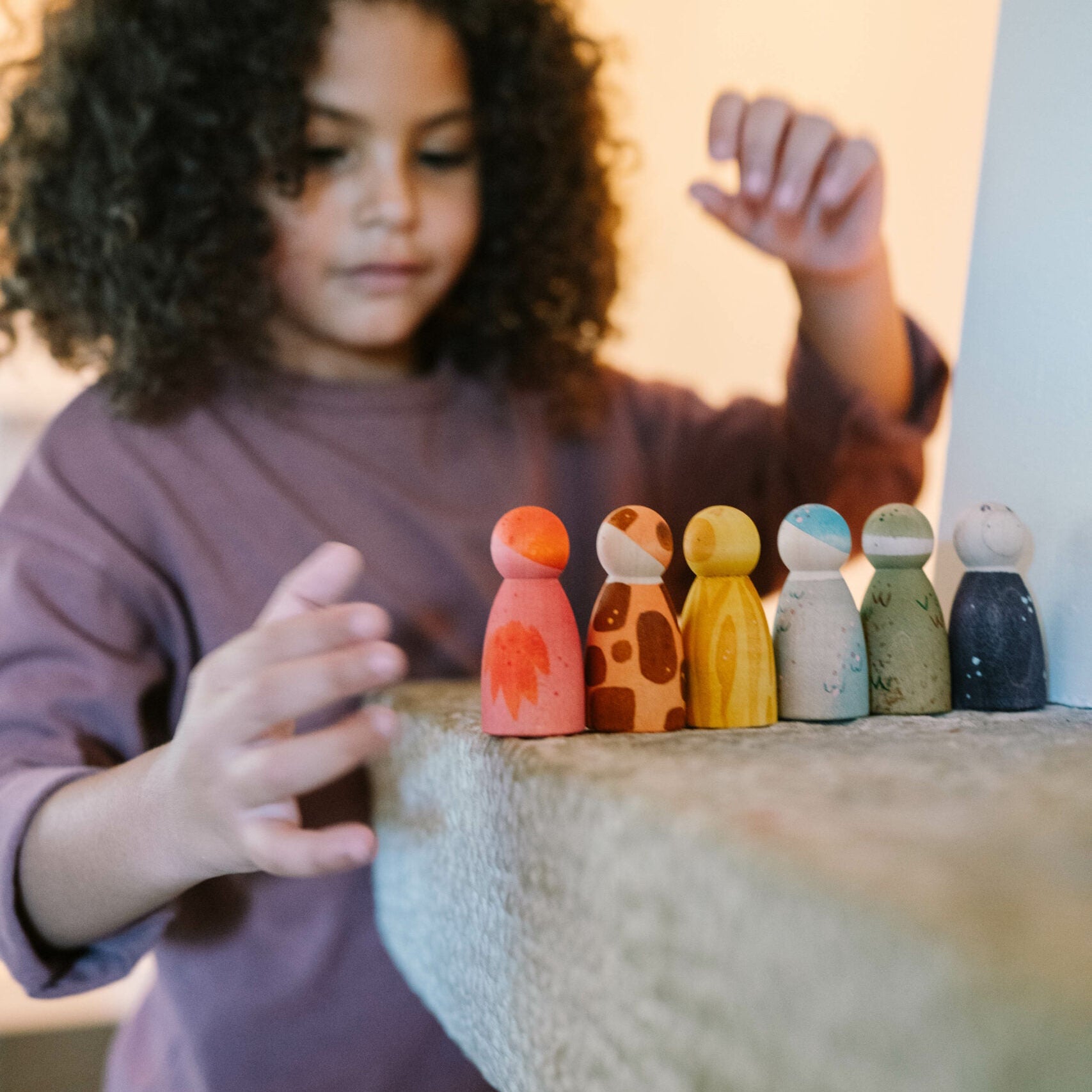 Child playing with colorful wooden peg dolls on a table.