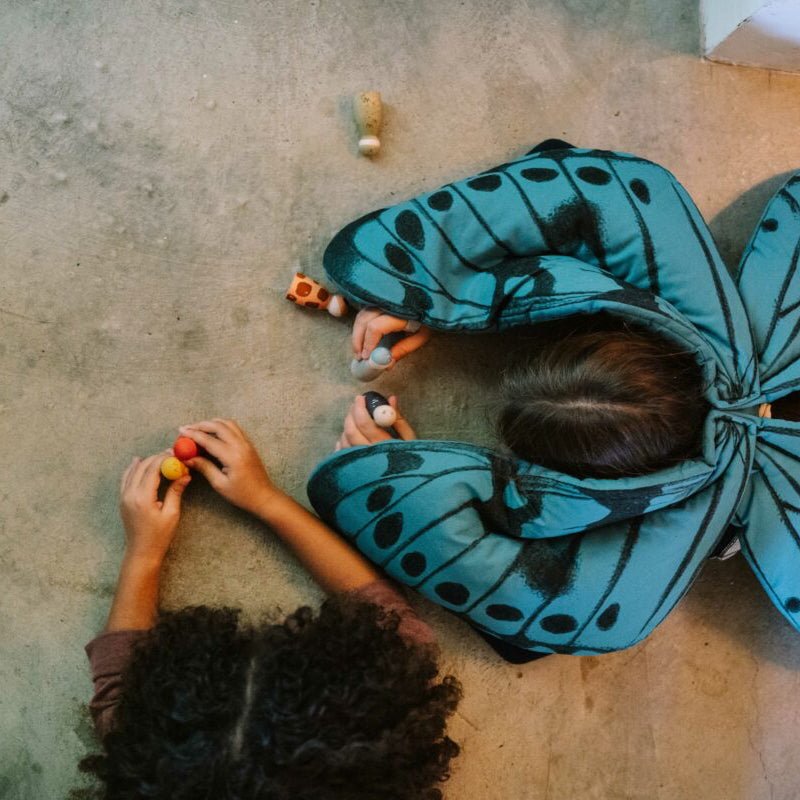 Person wearing a large blue butterfly costume on a concrete floor.