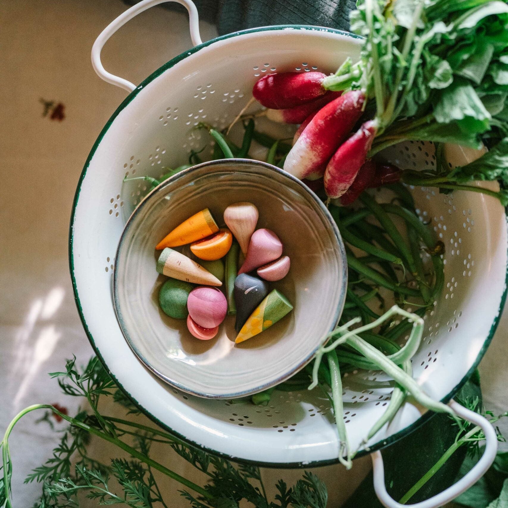 Colander with vegetables and a bowl of colorful candies on a table.