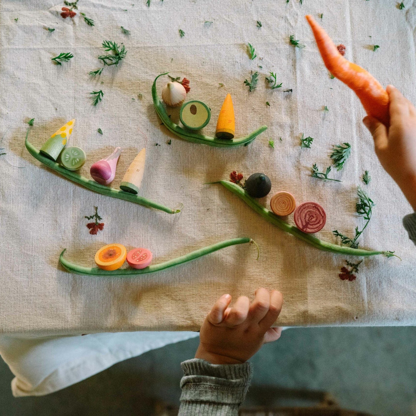 Person holding a carrot over a table with food art made of vegetables.