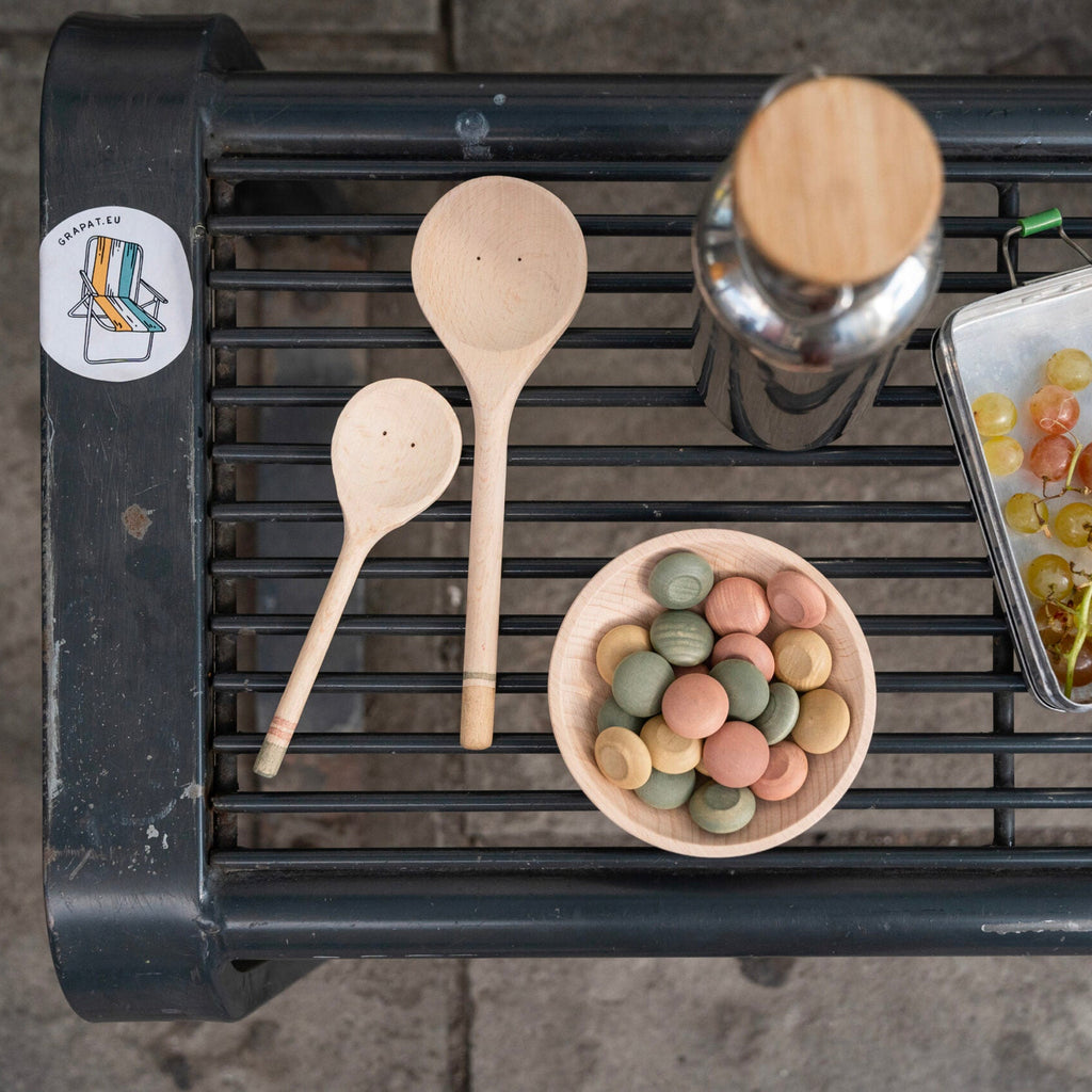 Wooden spoons, a bowl of colorful candies, and a container of grapes on a metal surface.