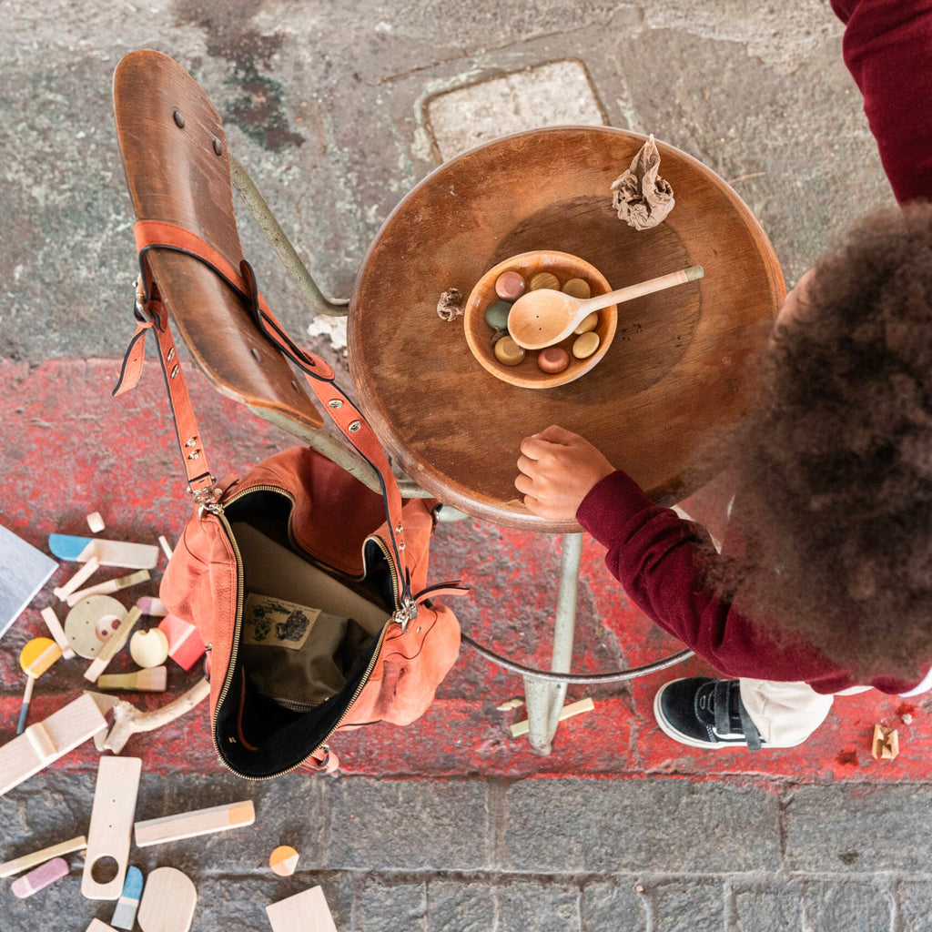 Person sitting at a table with a brown leather bag next to them on a street.