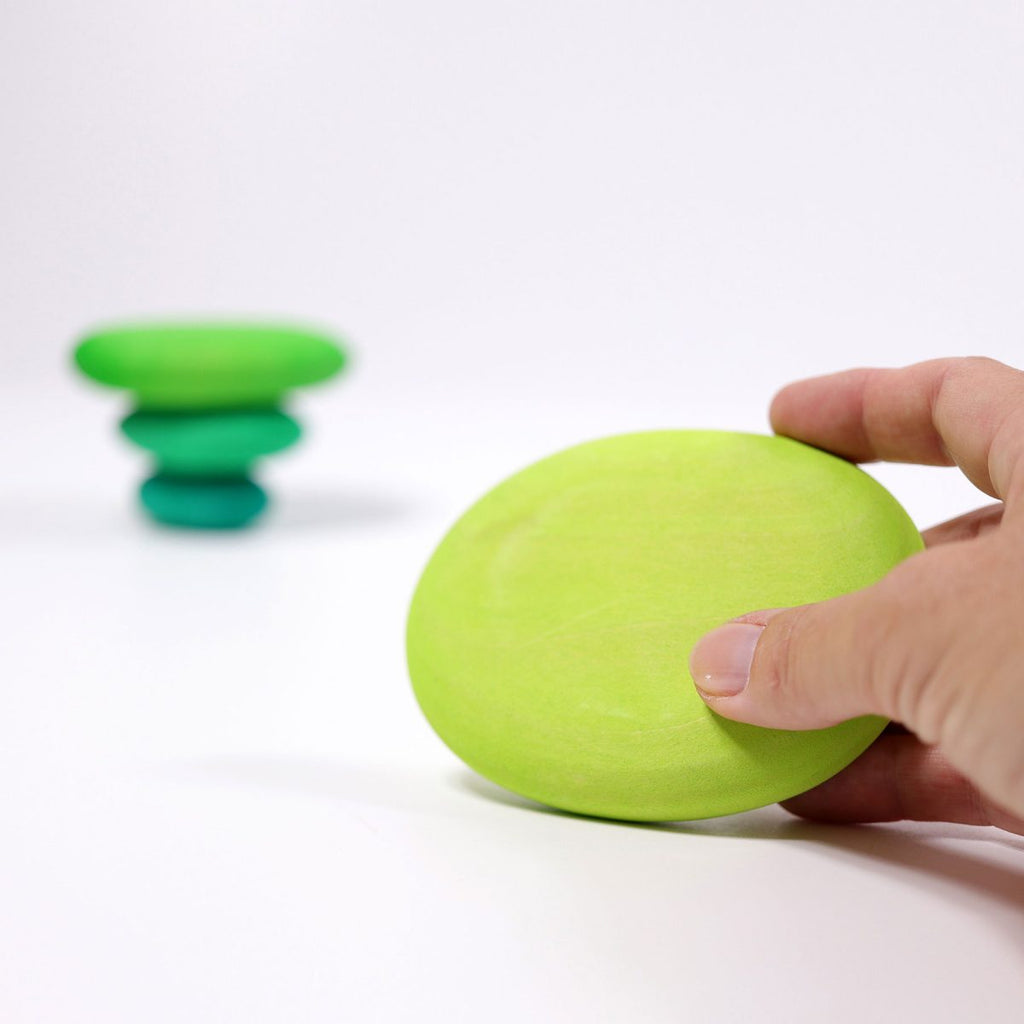 Hand holding a green pebble with another one in the background on a white surface