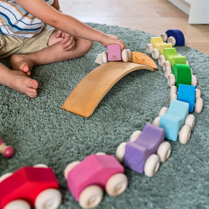 Children playing with a wooden toy train set on a rug