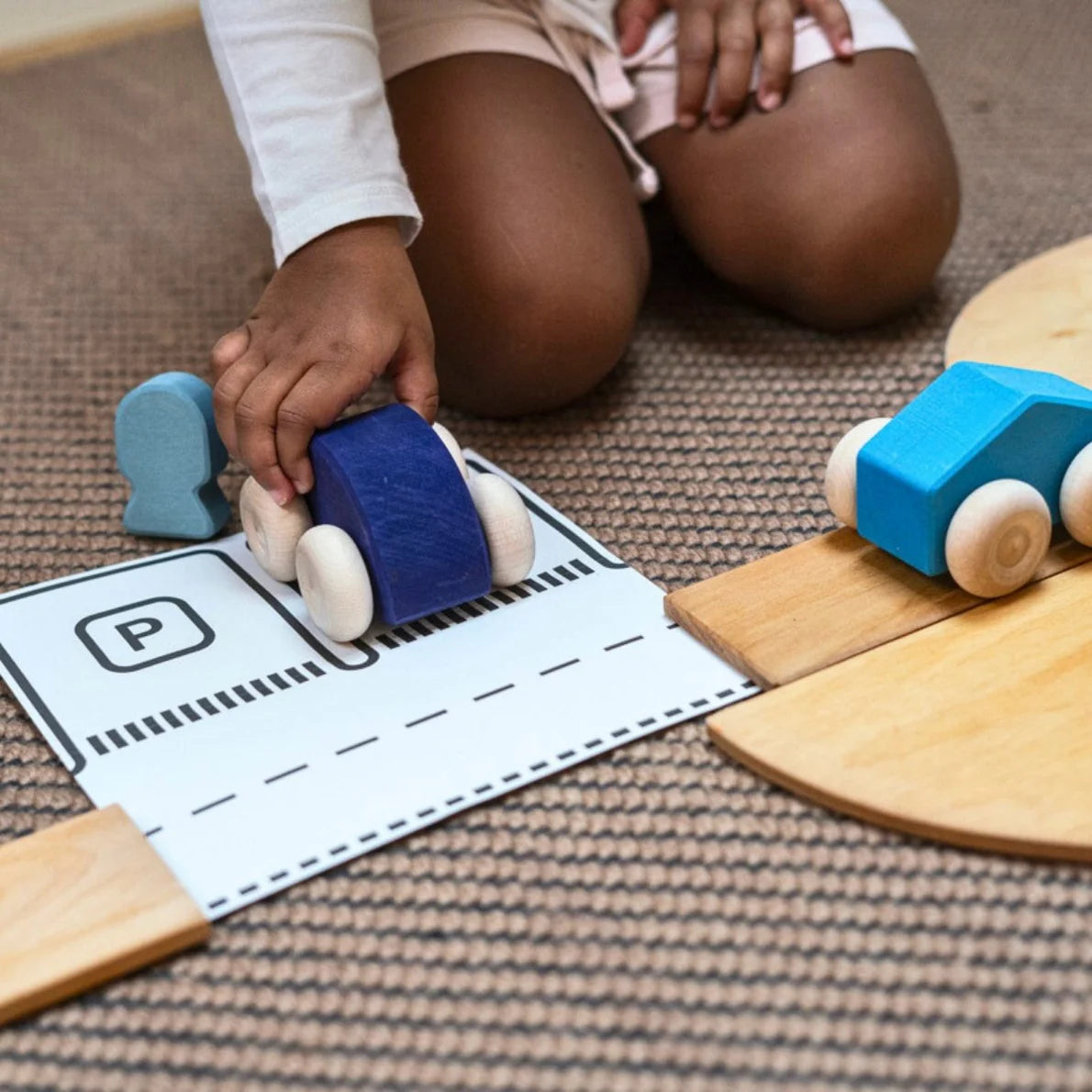 Child playing with toy cars on a wooden track and paper road map.