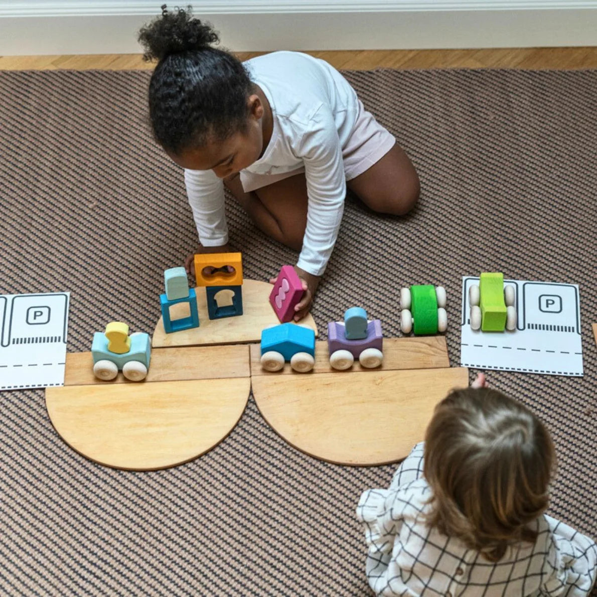 Two children playing with toy trains and blocks on a wooden track.