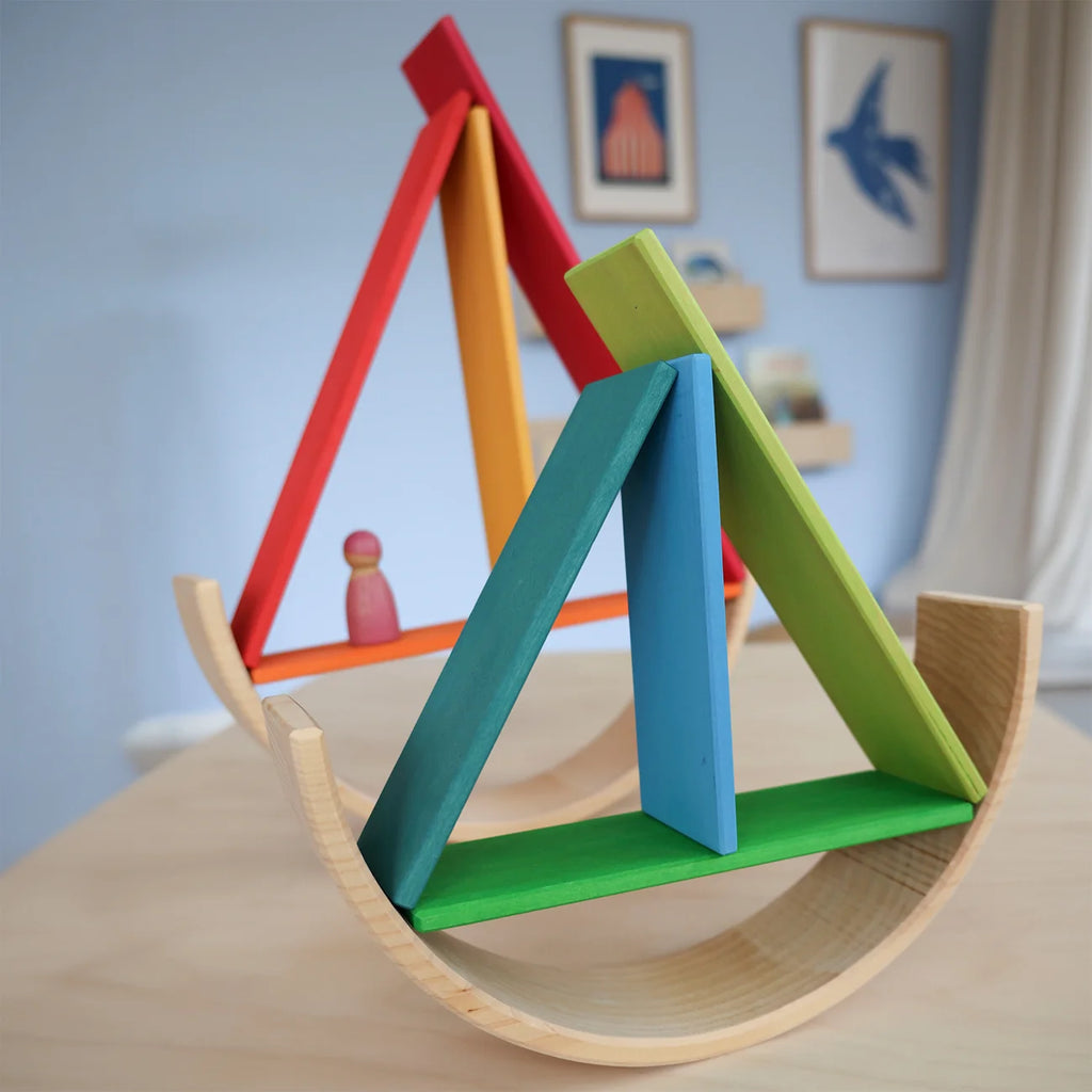 Colorful wooden toy structure on a table with a light blue wall and framed pictures in the background.