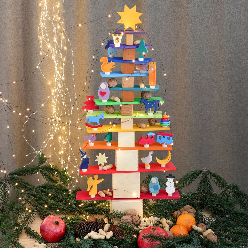 Decorative tower made of colorful blocks with small figurines on a bed of pine needles and lights.