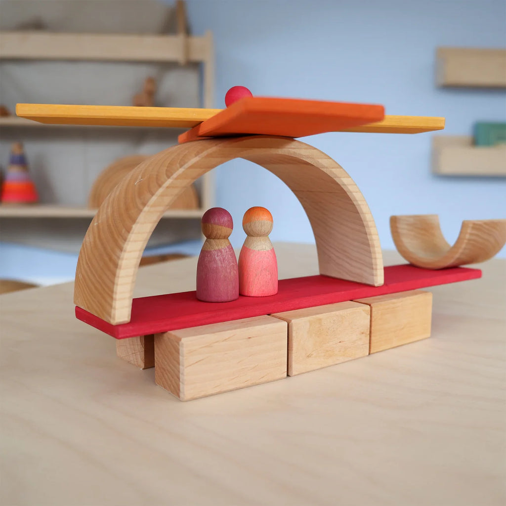 Wooden toy helicopter with red rotor and wooden figures on a wooden surface