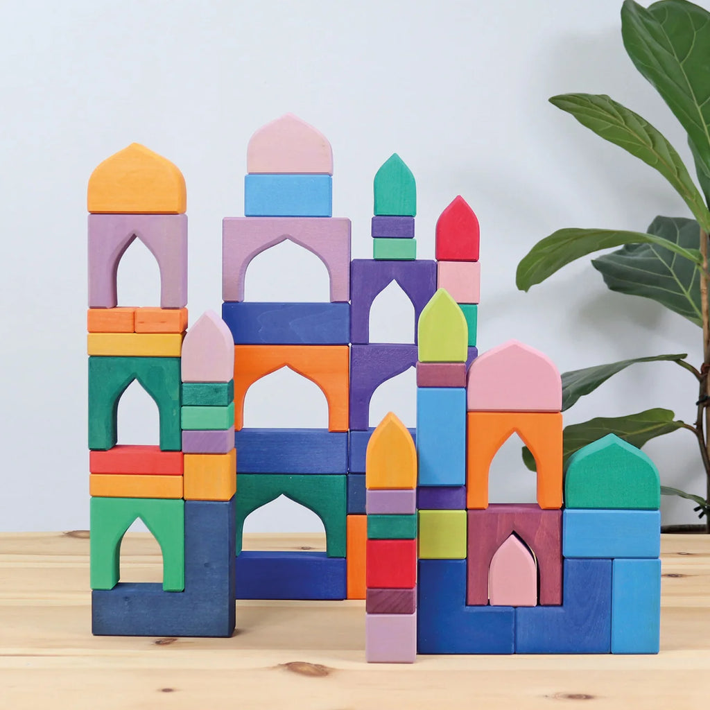 Colorful toy blocks stacked to resemble a castle on a wooden surface with a plant in the background.