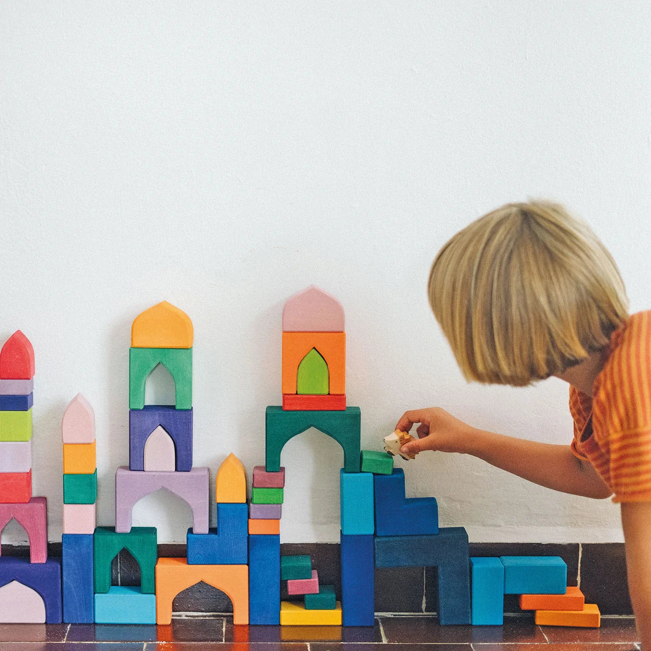 Child playing with colorful building blocks on a white floor.